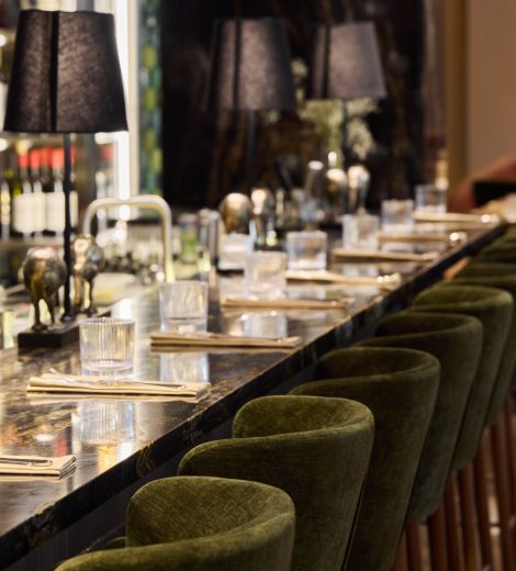 Row of green velvet bar stools along a marble restaurant counter.