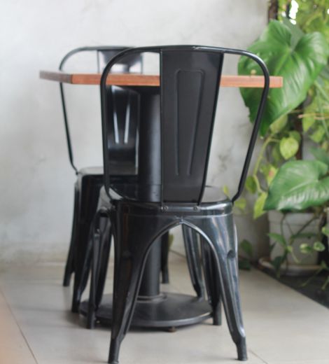Black metal chair and a wooden tabletop near greenery.