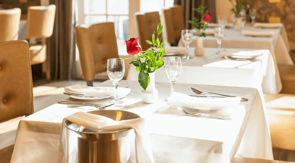 Classic dining table setting with white linens and red rose centerpiece.