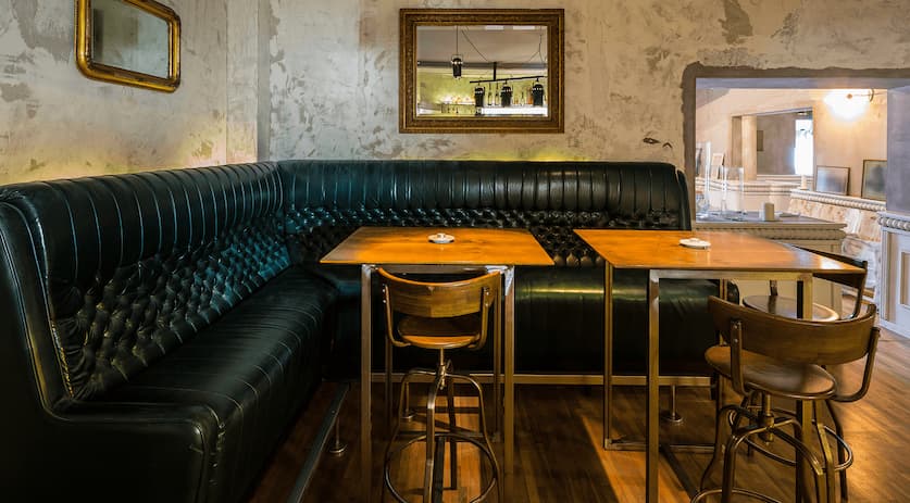 Tufted black vinyl L-shaped booth seating with wooden high-top tables and bar stools in a pub setting