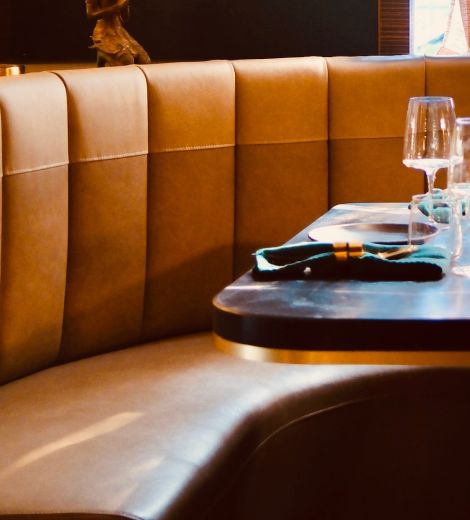 Curved tan leather booth seating beside a restaurant table set with glassware.